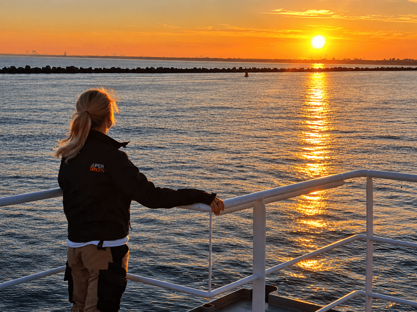 Maria Robakina at the railing of a vessel looking out over the water at sunset.